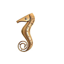 Load image into Gallery viewer, Gold-colored seahorse-shaped object on a textured gray surface